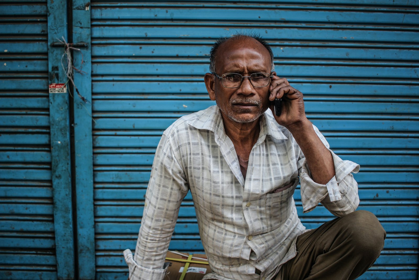 Indian man calling SBI India customer care on phone while seated in front of his shop.