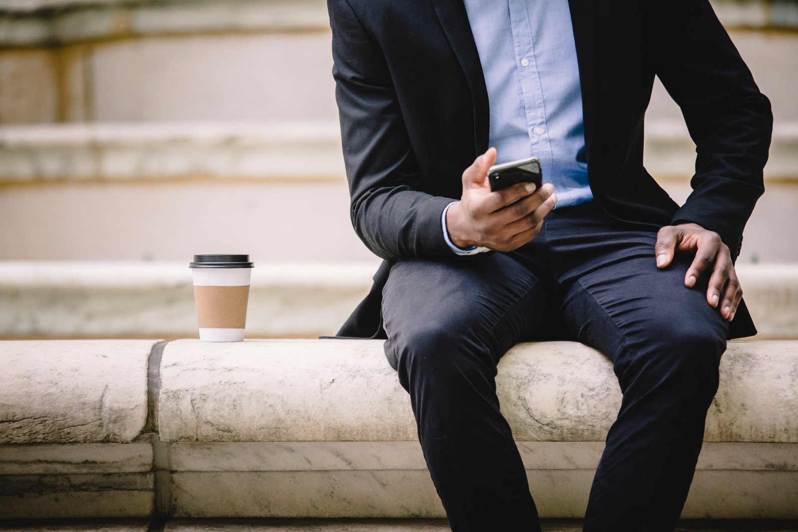 An employee resting on a bench with a take away coffee while using ICICI India SMS Banking Service on mobile phone.