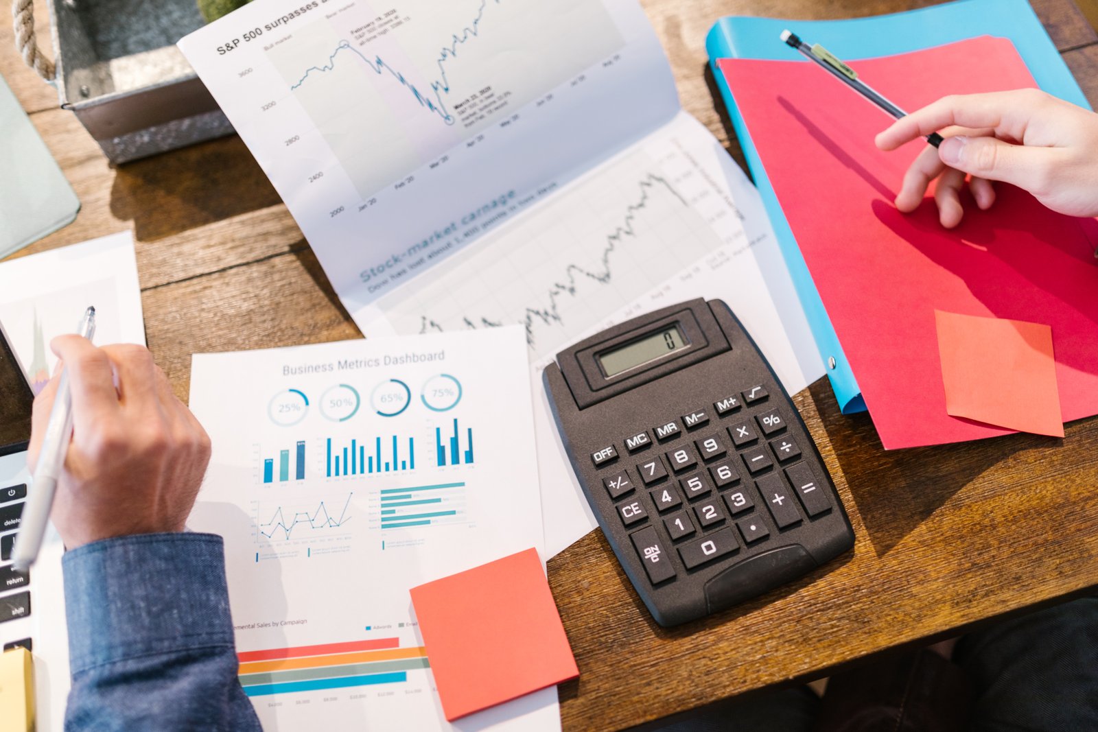 Two people calculating financial numbers with calculator on table surrounded by charts.