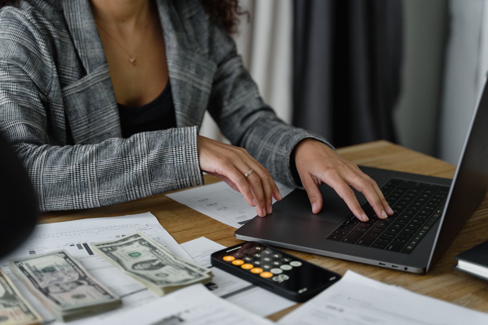 Woman using laptop and calculator with cash on table.