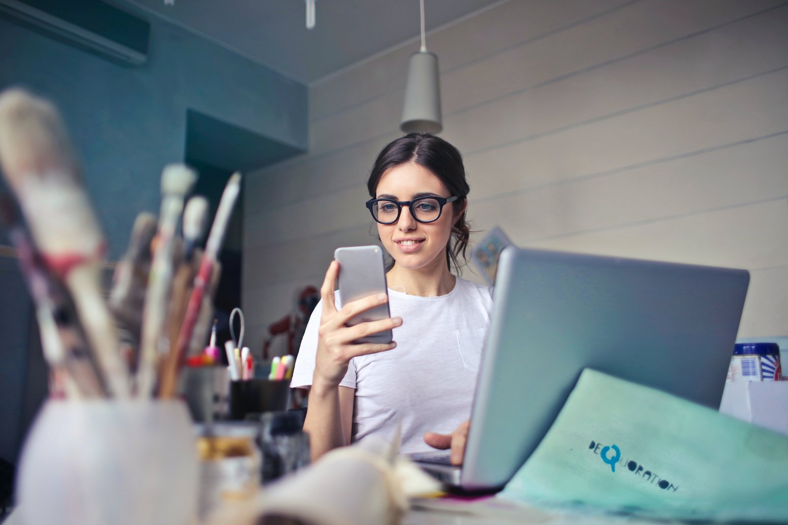 Woman dialing PhonePe Customer Care from her mobile phone with laptop in front.