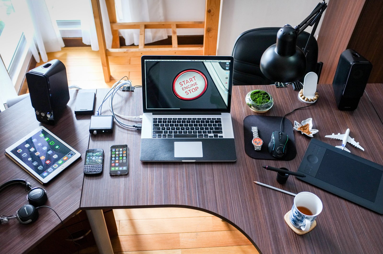 Brown Table with Arrangement of Electronic Devices including Laptop, Tablet, and Digital Camera.