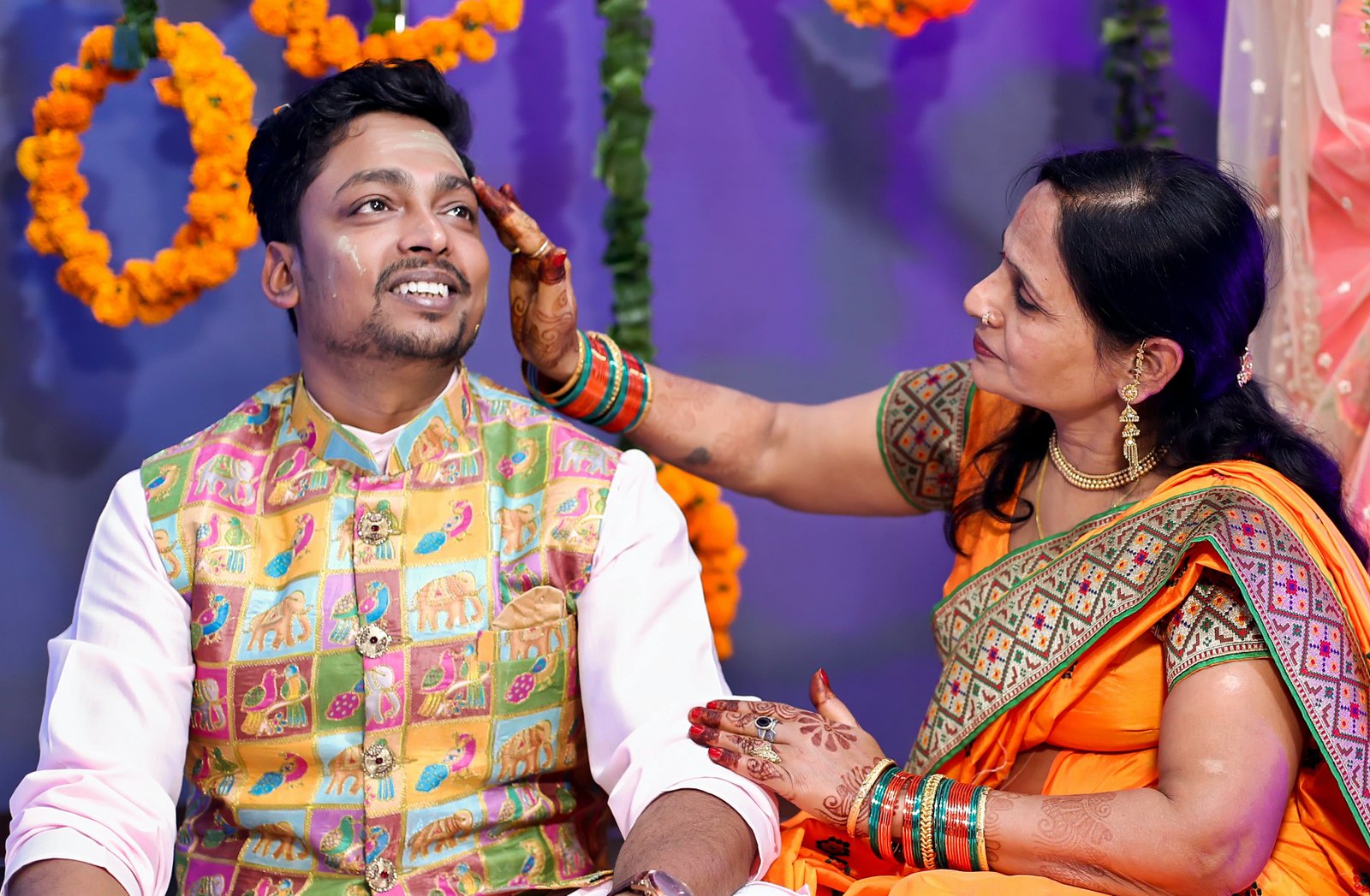 Indian mother applying turmeric to son's face during his wedding