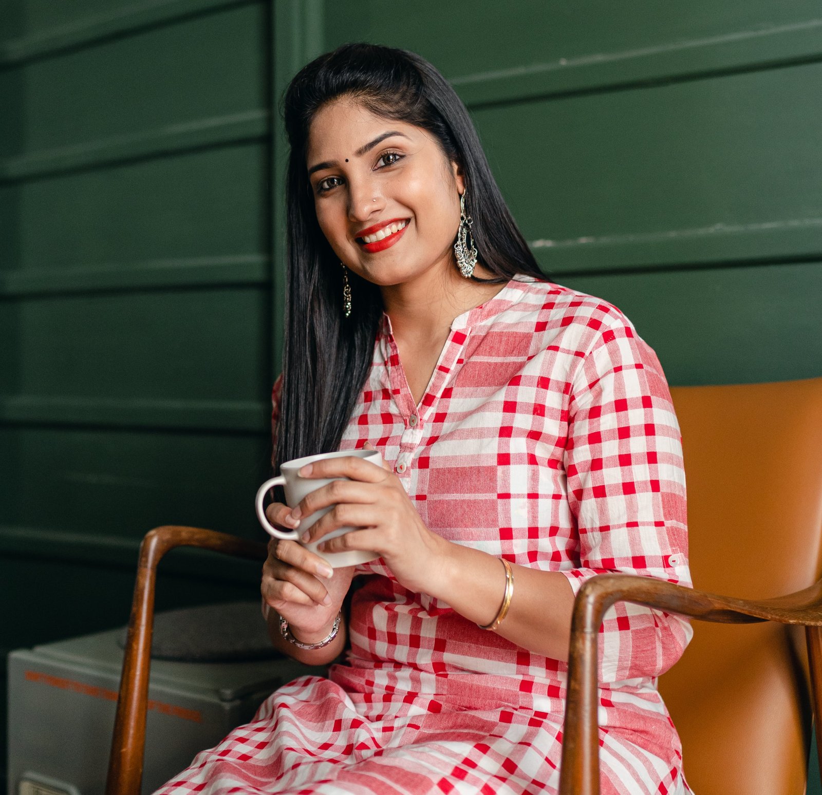 An Indian wife smiling and sitting on a chair and having chai in her hand