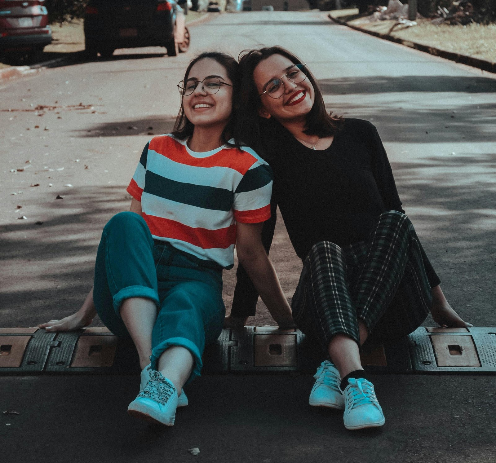 Two best friends who are girls laughing while sitting on the road bumper together